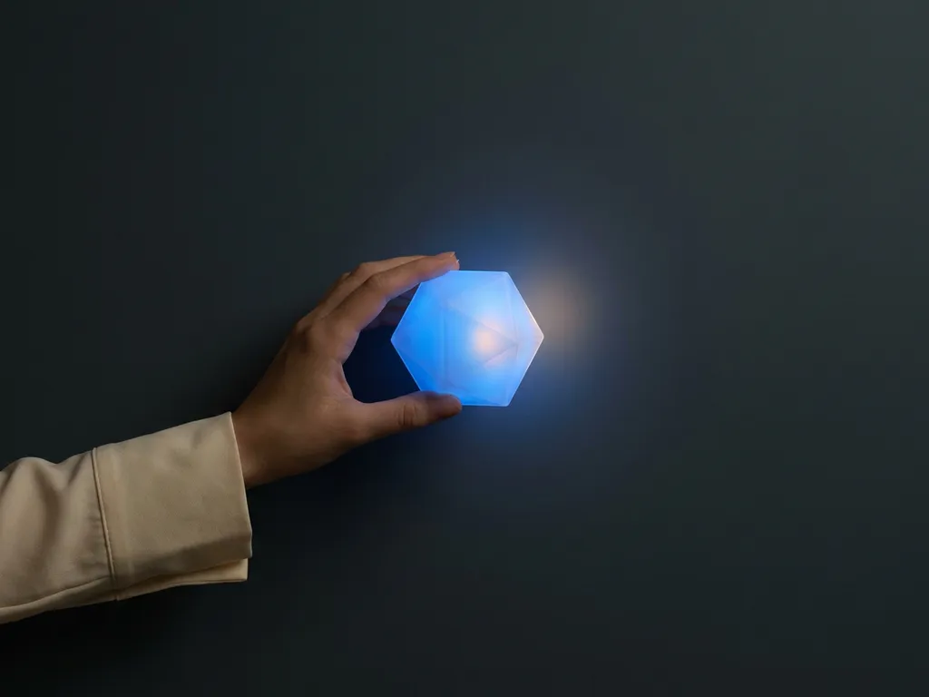 Fingertips touching a glowing blue geometric form floating in a dark minimalist space, blending physical and virtual worlds.