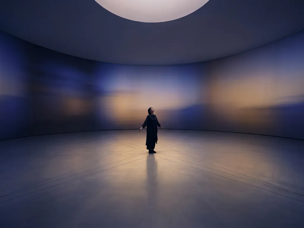Person standing in a vast circular room with indigo and amber light gradients radiating across curved minimalist walls.